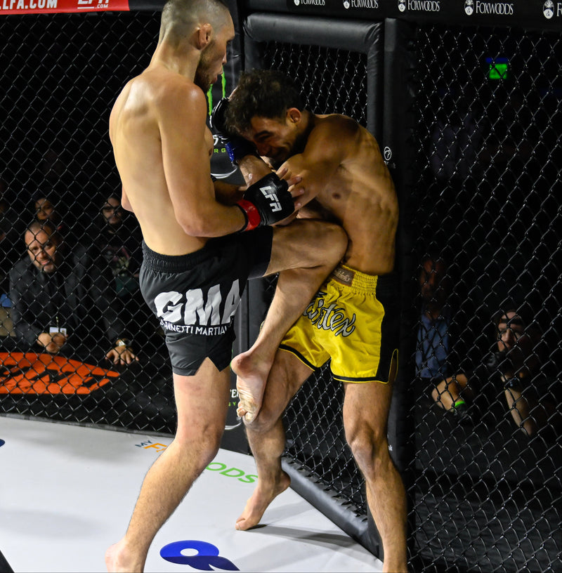 Two male fighters in an MMA octagon cage, with one in black shorts delivering a punch to the other in yellow shorts. Visible brands include GMA, Bonzi Pure, and LFA on the mat and cage.